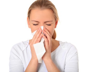 Eine junge Frau putzt sich mit einem Taschentuch die Nase