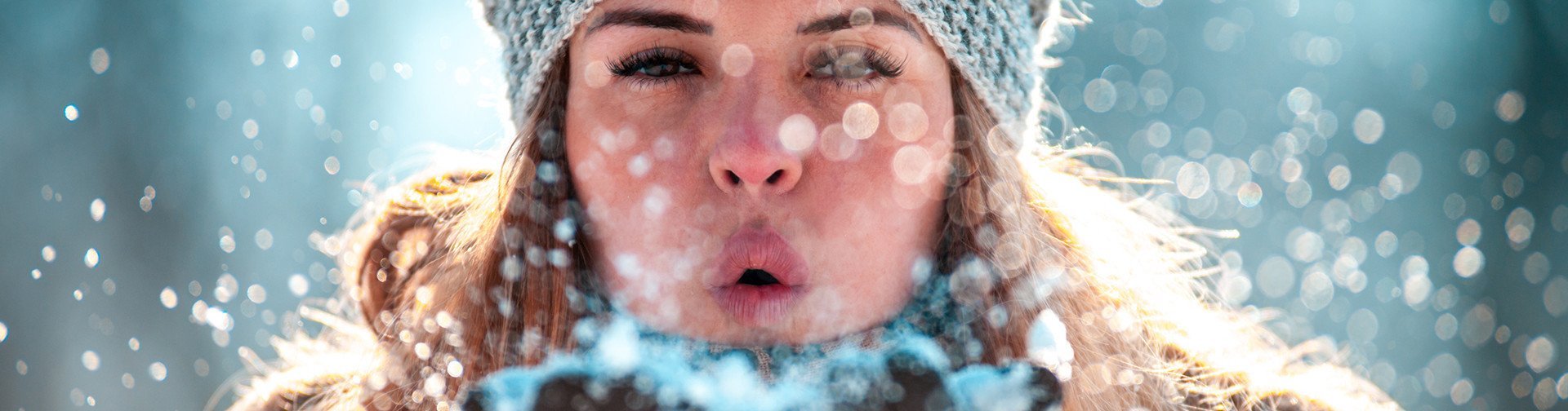 Frau mit Mütze pustet Schnee in die Kamera